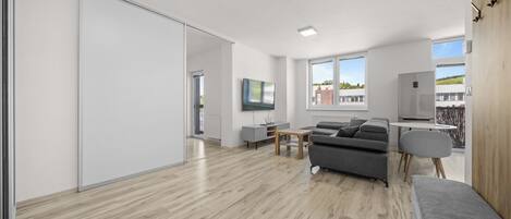 A modern living space with a sliding door, a grey sofa, a small table, and a view of the outside.