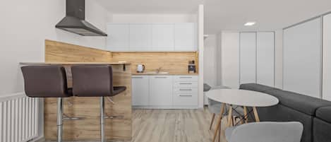 A modern kitchen with white cabinets, a wooden accent wall, a black range hood, and a dining area with a grey sofa and two chairs.