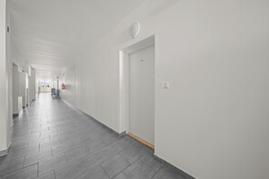 Een lange, smalle gang met betegelde vloer en witte muren.