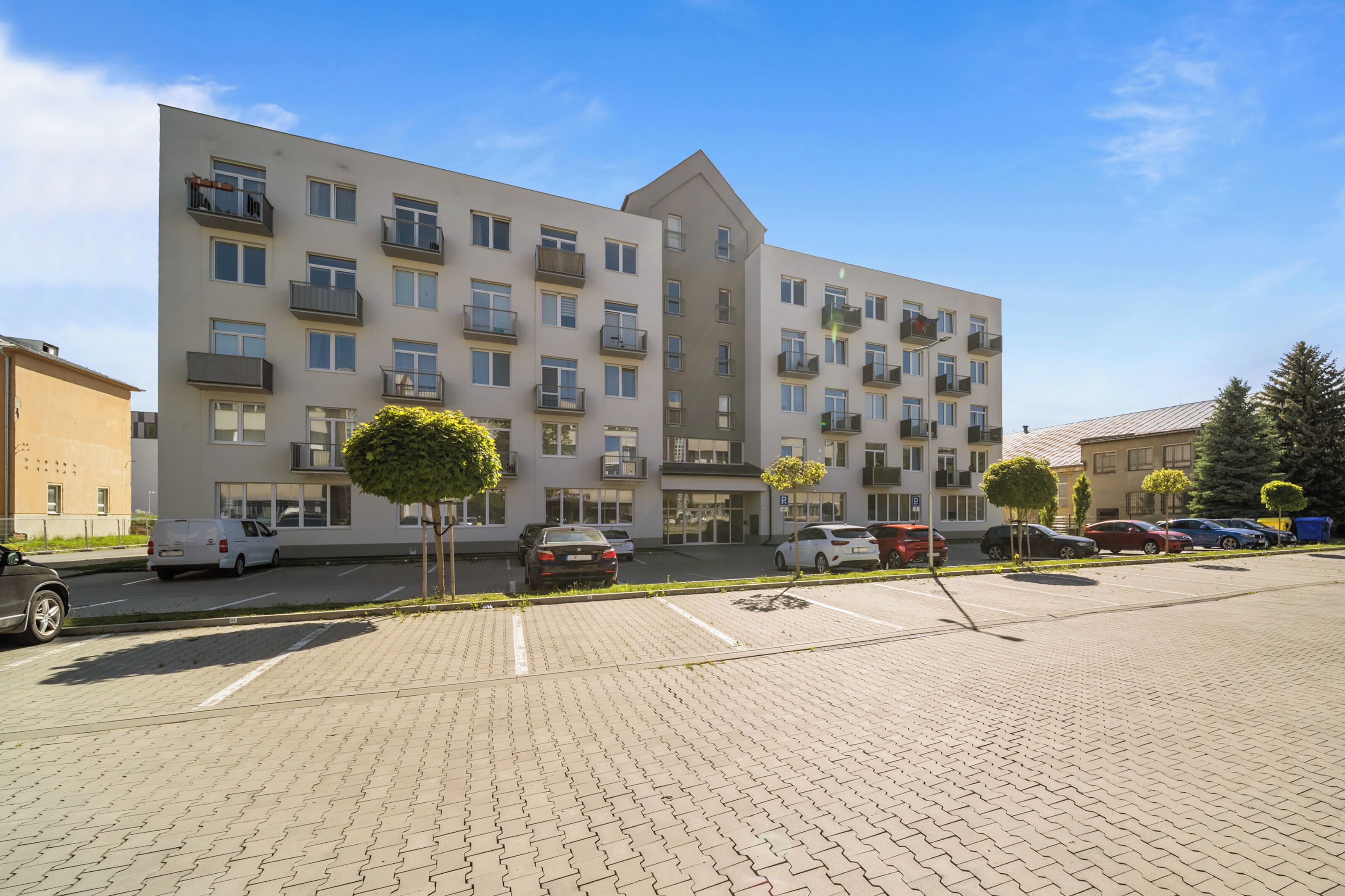 Un edificio residencial de varios pisos con balcones, estacionamiento y cielo despejado.