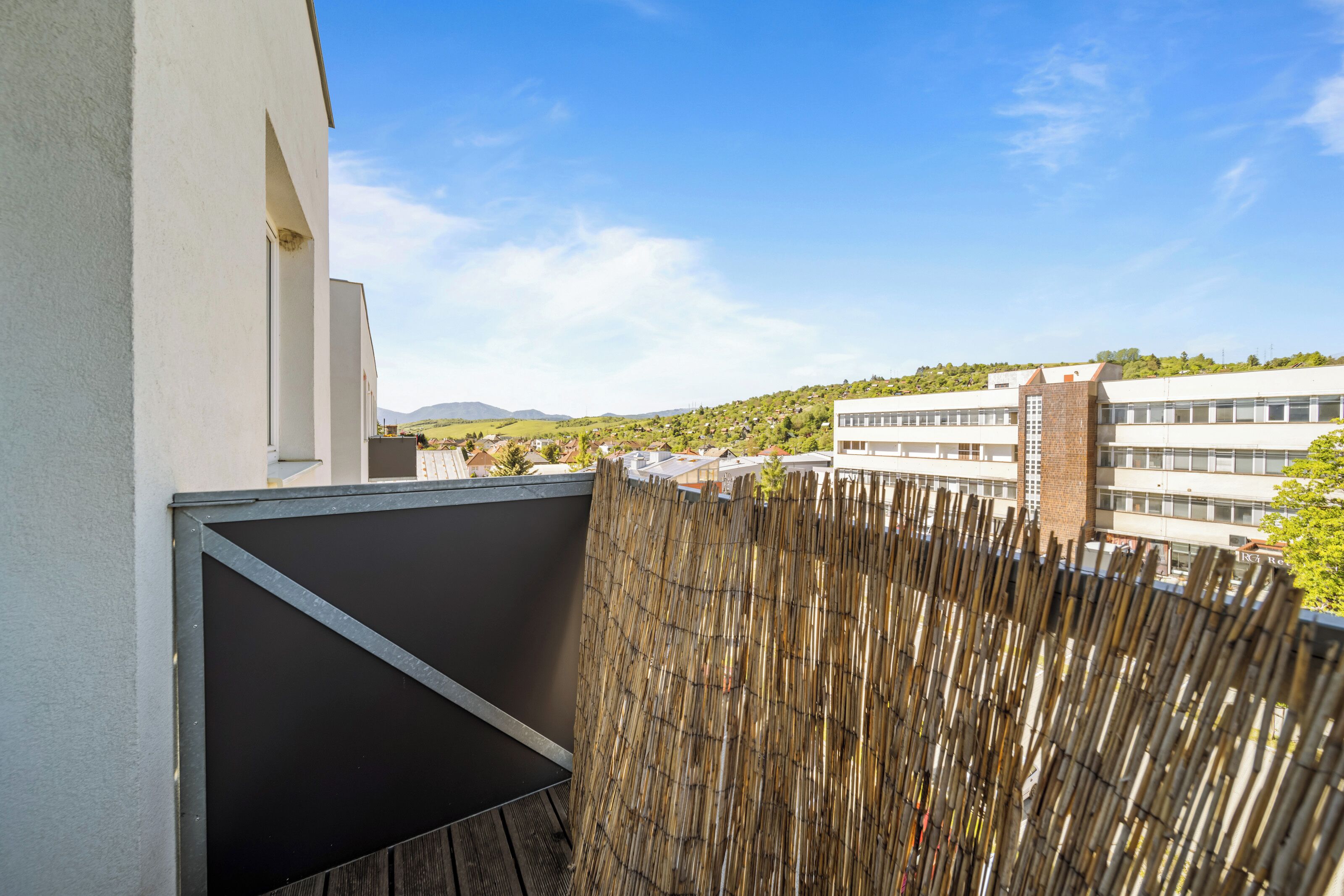A balcony with a view of a residential area, a bamboo fence, and a building with multiple windows.