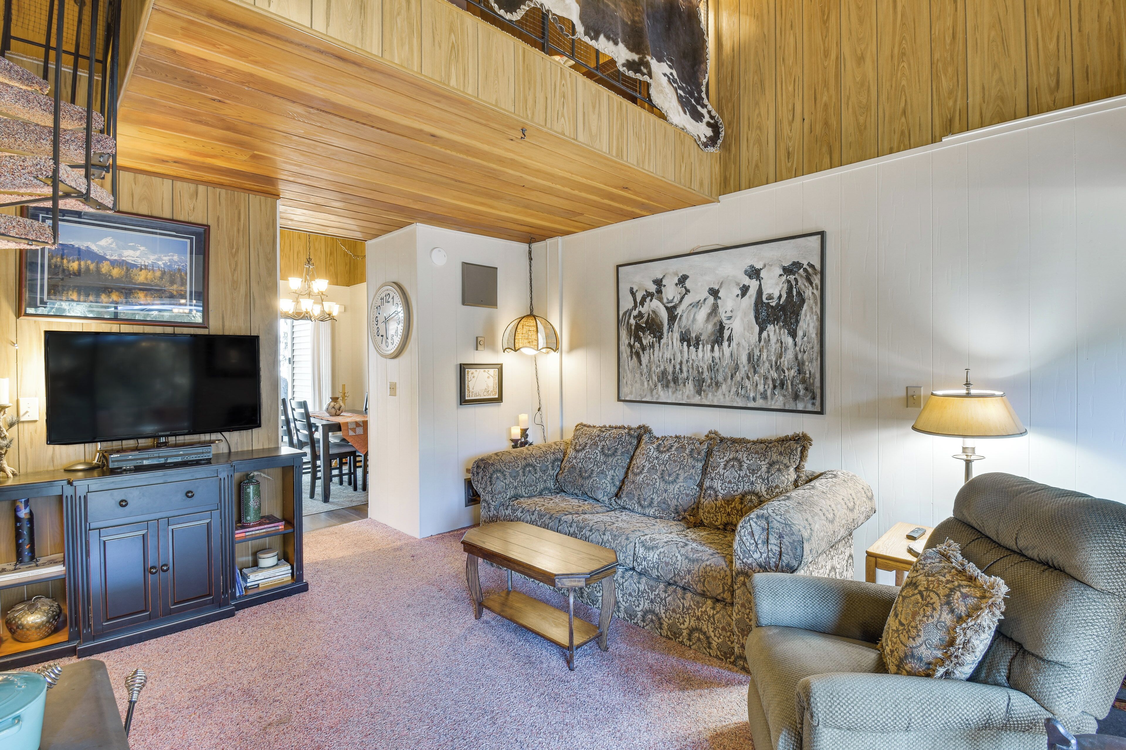 A cozy living room with a television, sofa, and a painting of cows.