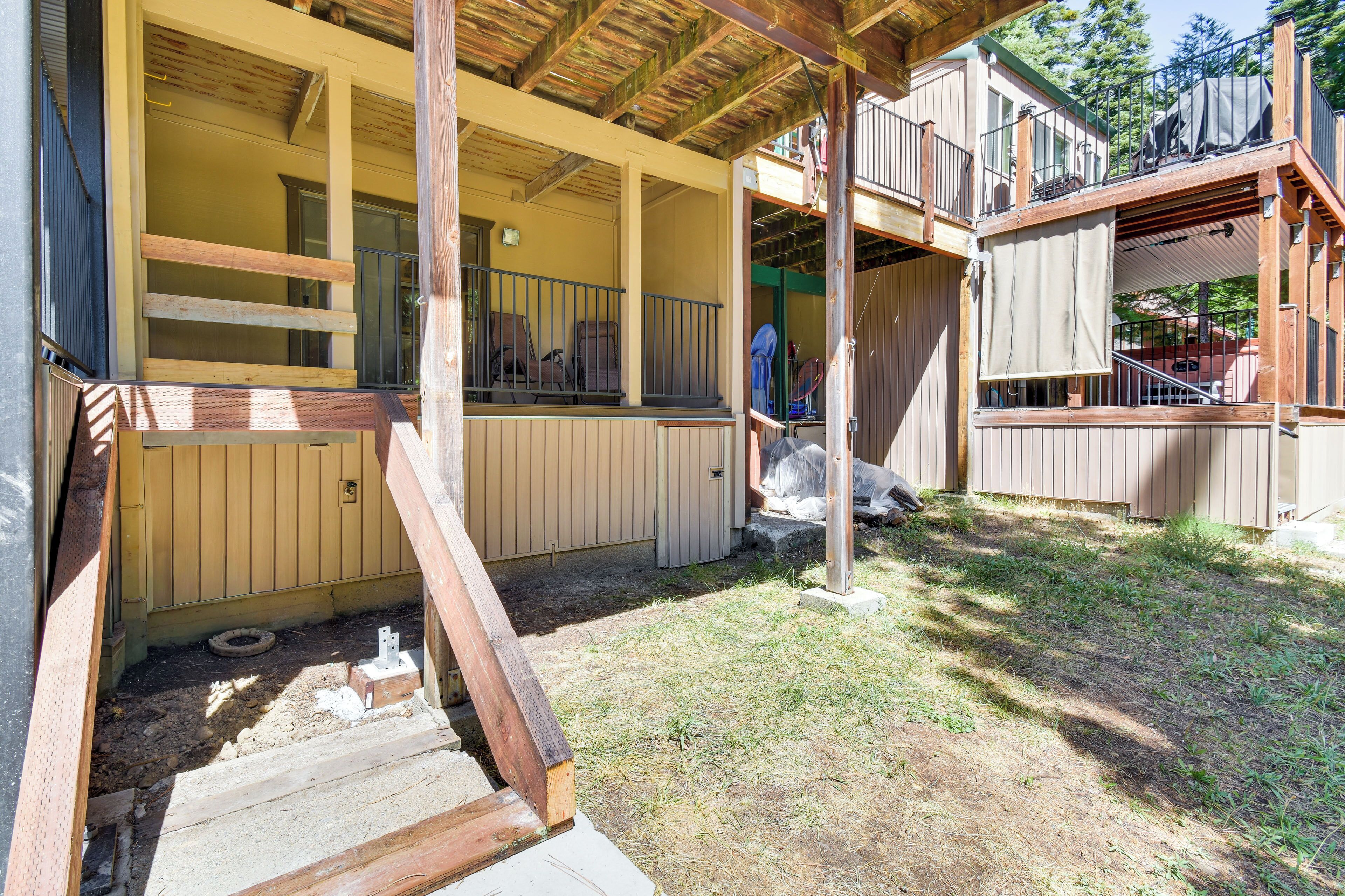A covered outdoor area with a wooden deck, a covered seating area, and a staircase leading to a higher level.