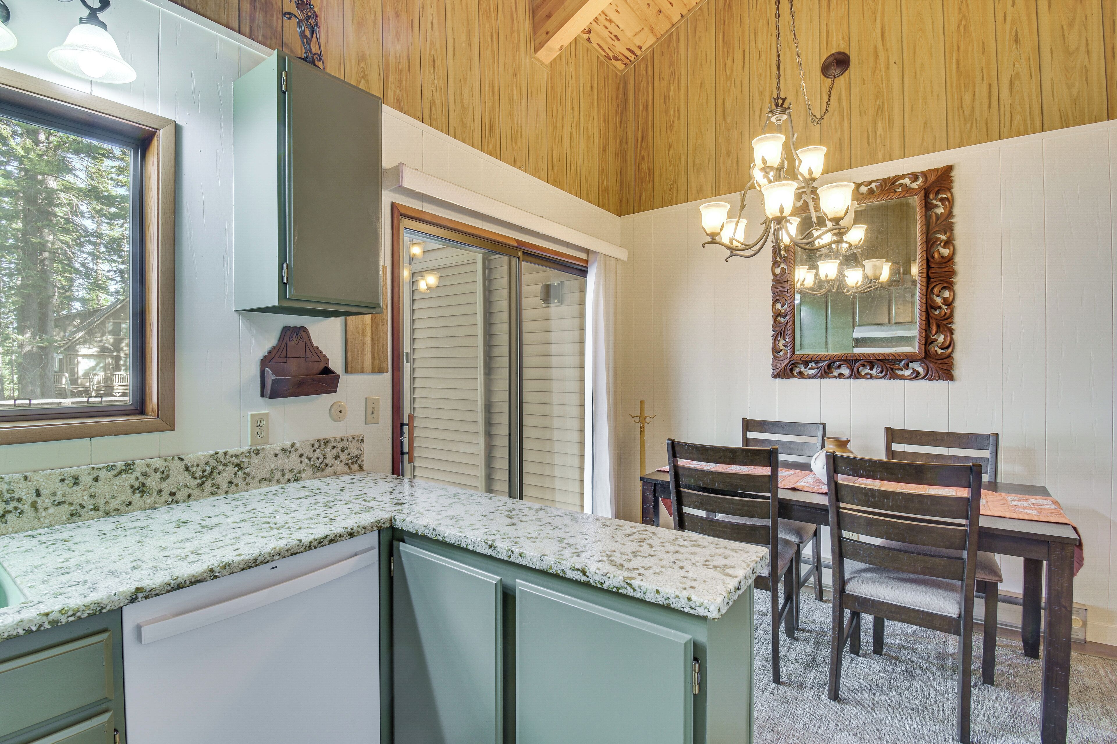 A kitchen with a granite countertop, wooden cabinets, a dining table with chairs, and a chandelier.