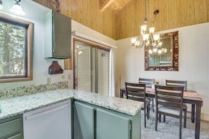 A kitchen with a granite countertop, wooden cabinets, a dining table with chairs, and a chandelier.