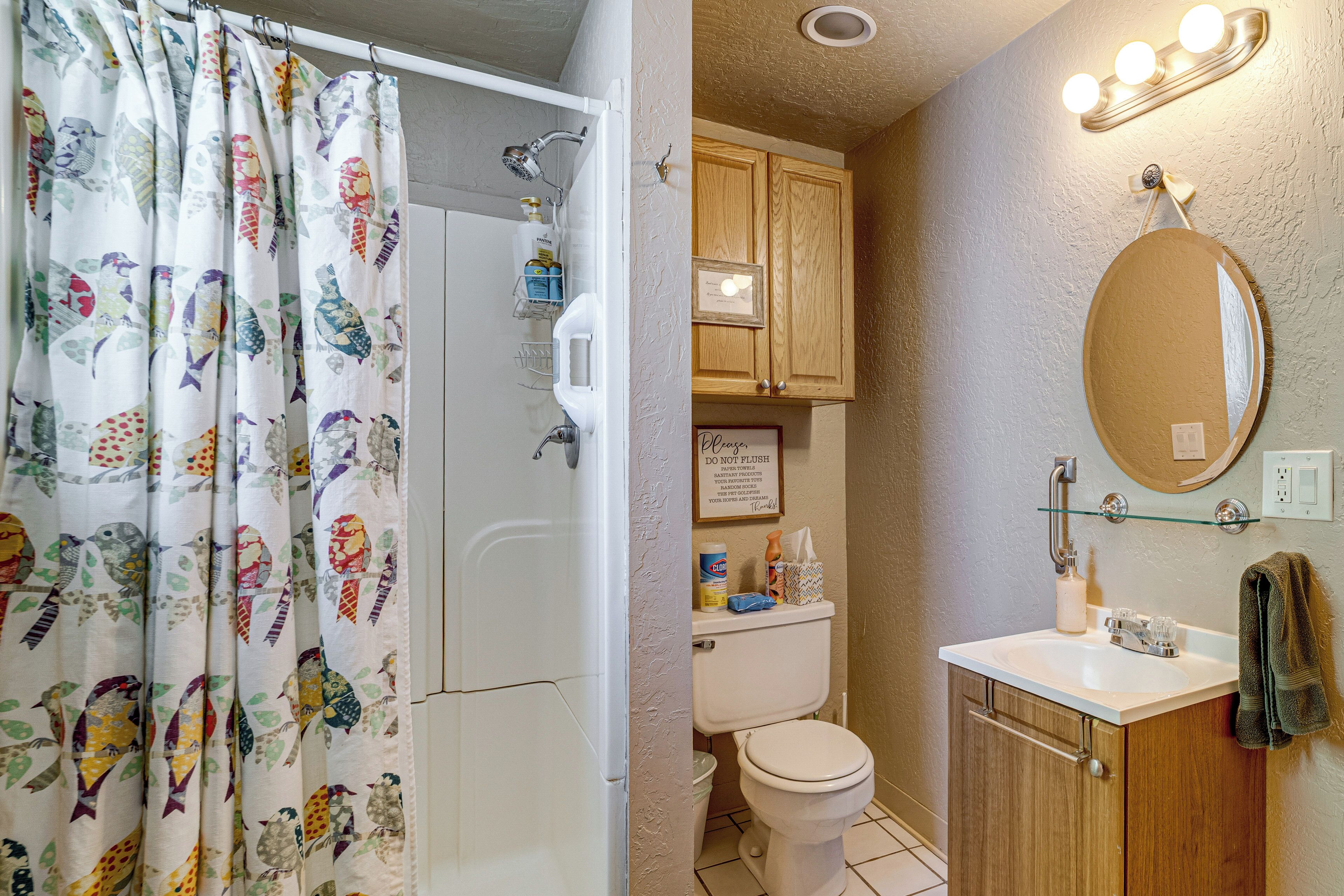 Baño con ducha, inodoro, lavamanos y espejo.