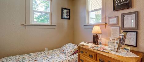 A bedroom with a bed, dresser, and two windows.