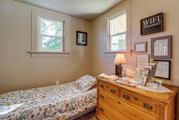 A bedroom with a bed, dresser, and two windows.