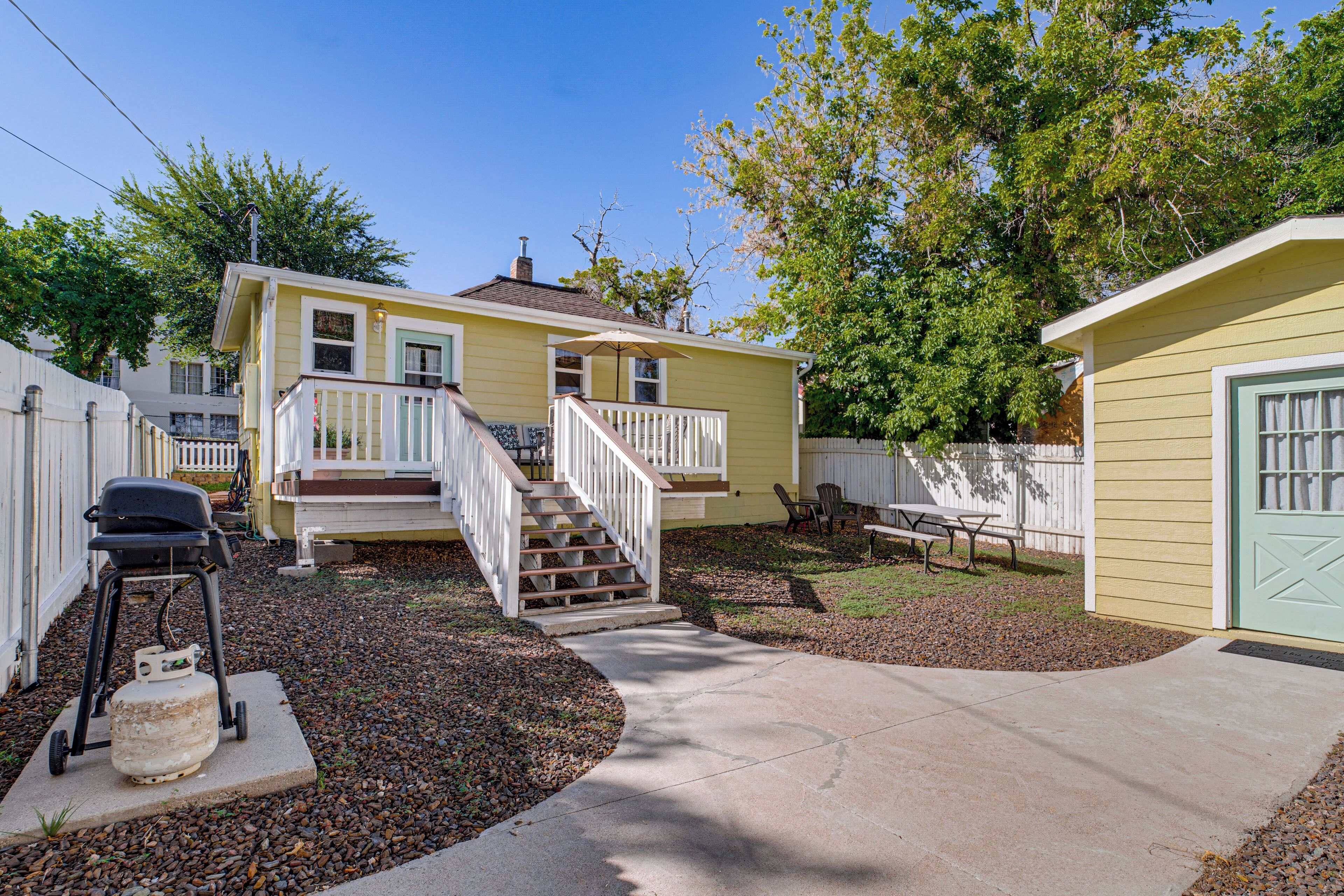 A residential property with a front porch, a staircase leading to a deck, a barbecue grill, and a small shed.