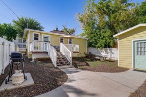 A residential property with a front porch, a staircase leading to a deck, a barbecue grill, and a small shed.