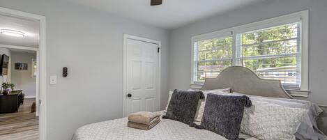 A bedroom with a bed, a ceiling fan, a window, and a door.