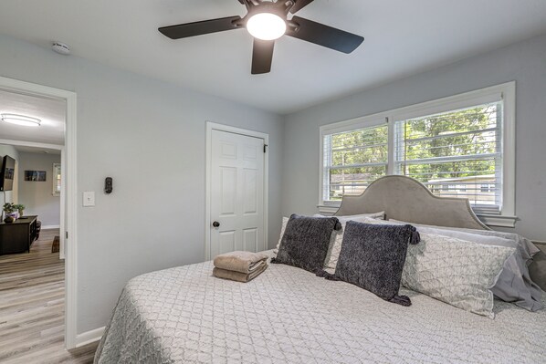 A bedroom with a bed, a ceiling fan, a window, and a door.