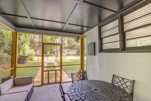 A covered patio with a glass door leading to a grassy yard, a round metal table, and a white sofa.