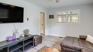 A living room with a flat-screen TV, a ceiling fan, a window with blinds, and a brown leather sofa. - Walk to FSU Campus & Stadium! Tallahassee Home (Tallahassee)
