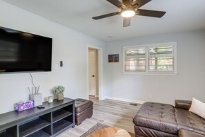 A living room with a flat-screen TV, a ceiling fan, a window with blinds, and a brown leather sofa. - Walk to FSU Campus & Stadium! Tallahassee Home (Tallahassee)