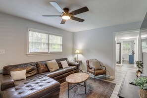 A living room with a leather sofa, a round coffee table, a chair, a floor lamp, and a ceiling fan.