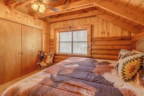 Ein Schlafzimmer in einer Blockhütte mit einem Bett, einem Fenster und einem Deckenventilator.