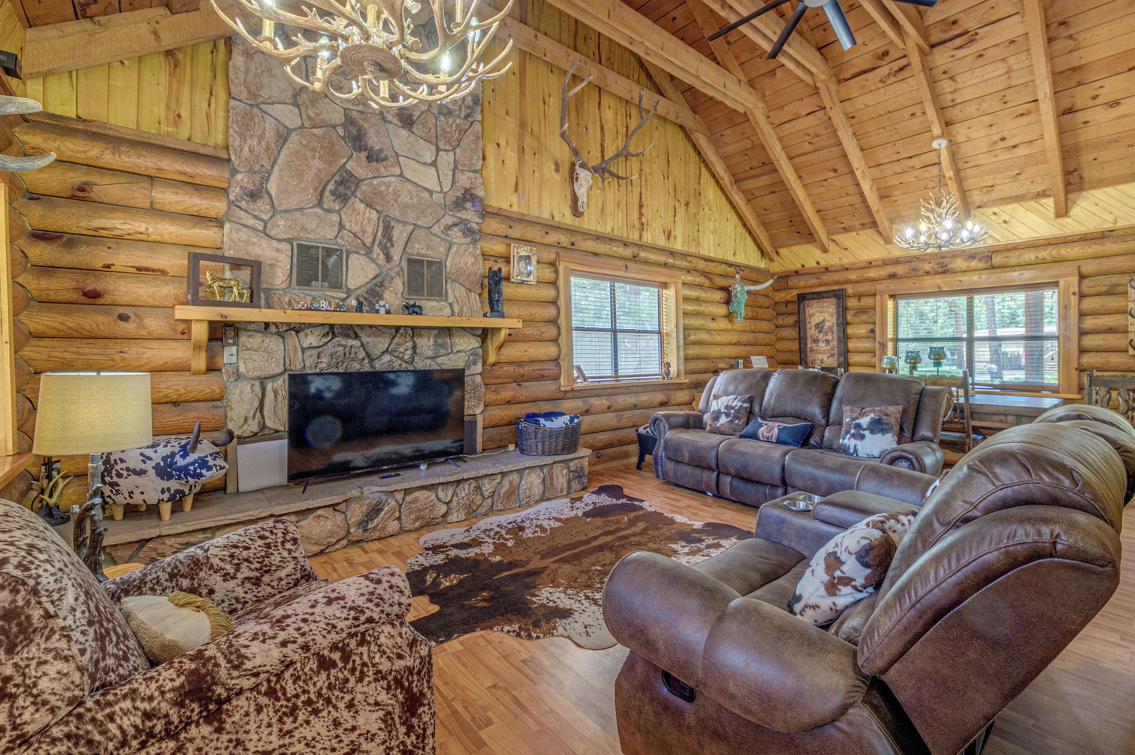 A log cabin interior with a stone fireplace, leather sofas, and a television.
