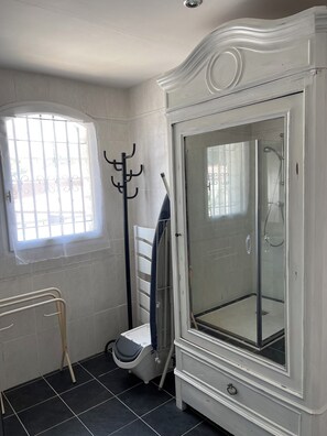 Une salle de bain avec un meuble blanc, une cabine de douche en verre, une fenêtre avec des barreaux et un porte-serviettes.