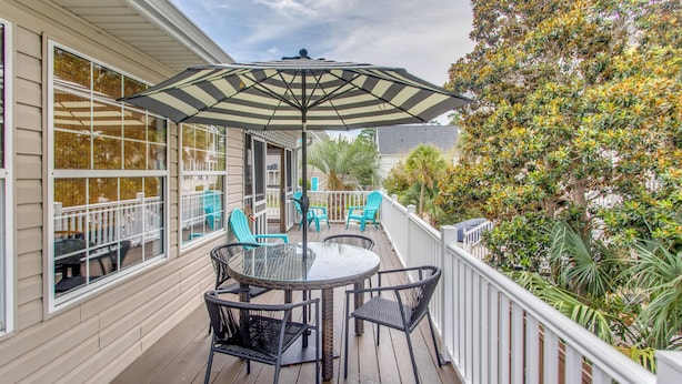 A covered outdoor patio with a table and chairs, a striped umbrella, and a view of a house and trees. - Ocean-view Retreat Near Barefoot Landing & Beach! (Myrtle Beach)