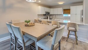 A modern kitchen with white cabinets, a dining table with six chairs, and a pendant light fixture. - Ocean-view Retreat Near Barefoot Landing & Beach! (Myrtle Beach)