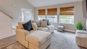 A living room with a beige sectional sofa, a ceiling fan, and a large window with blinds. - Ocean-view Retreat Near Barefoot Landing & Beach! (Myrtle Beach)