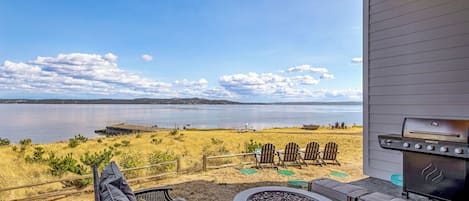 A patio with outdoor seating, a fire pit, and a grill overlooking a lake.