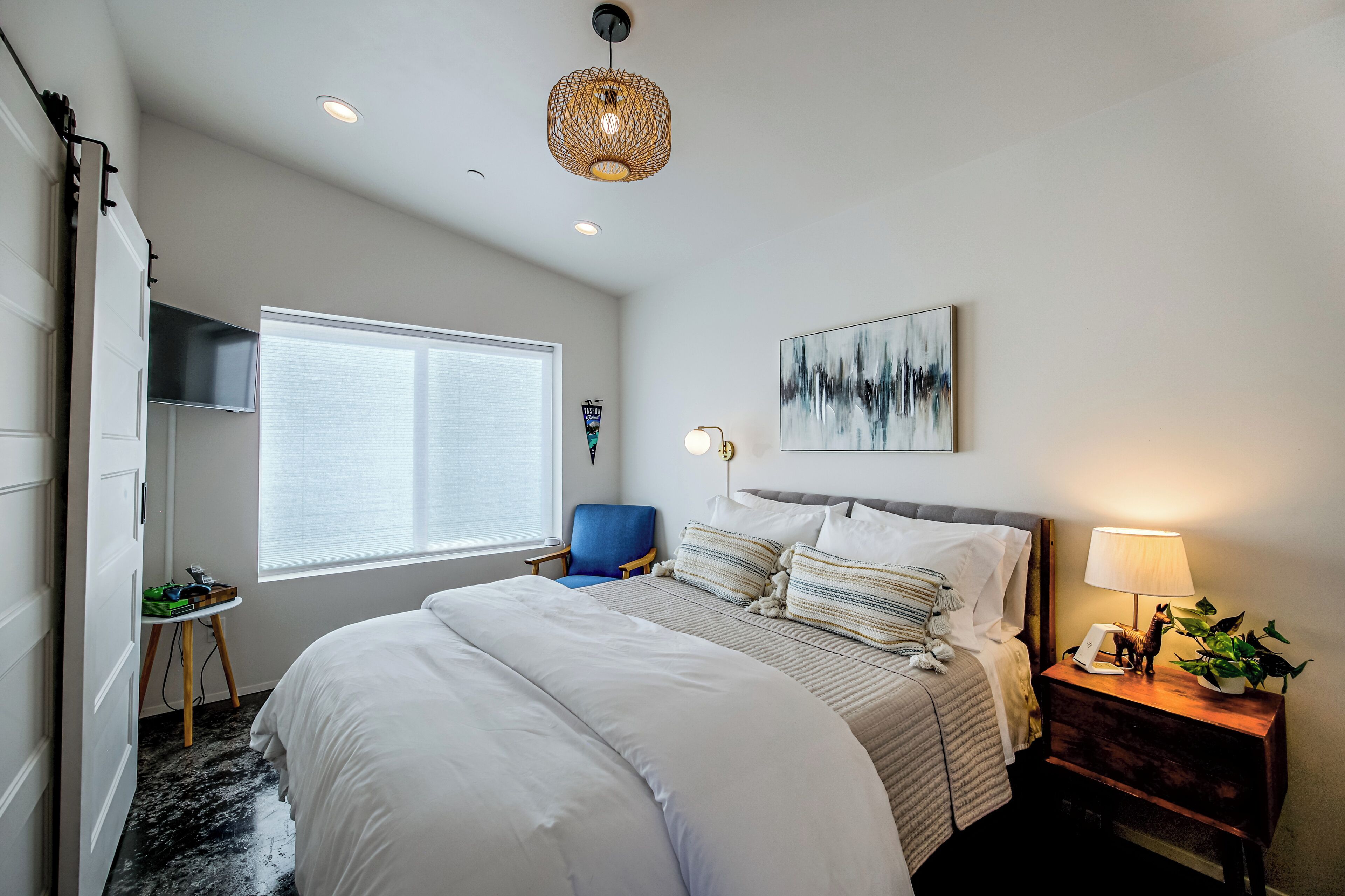 A bedroom with a large bed, a desk, a chair, a lamp, and a painting on the wall.