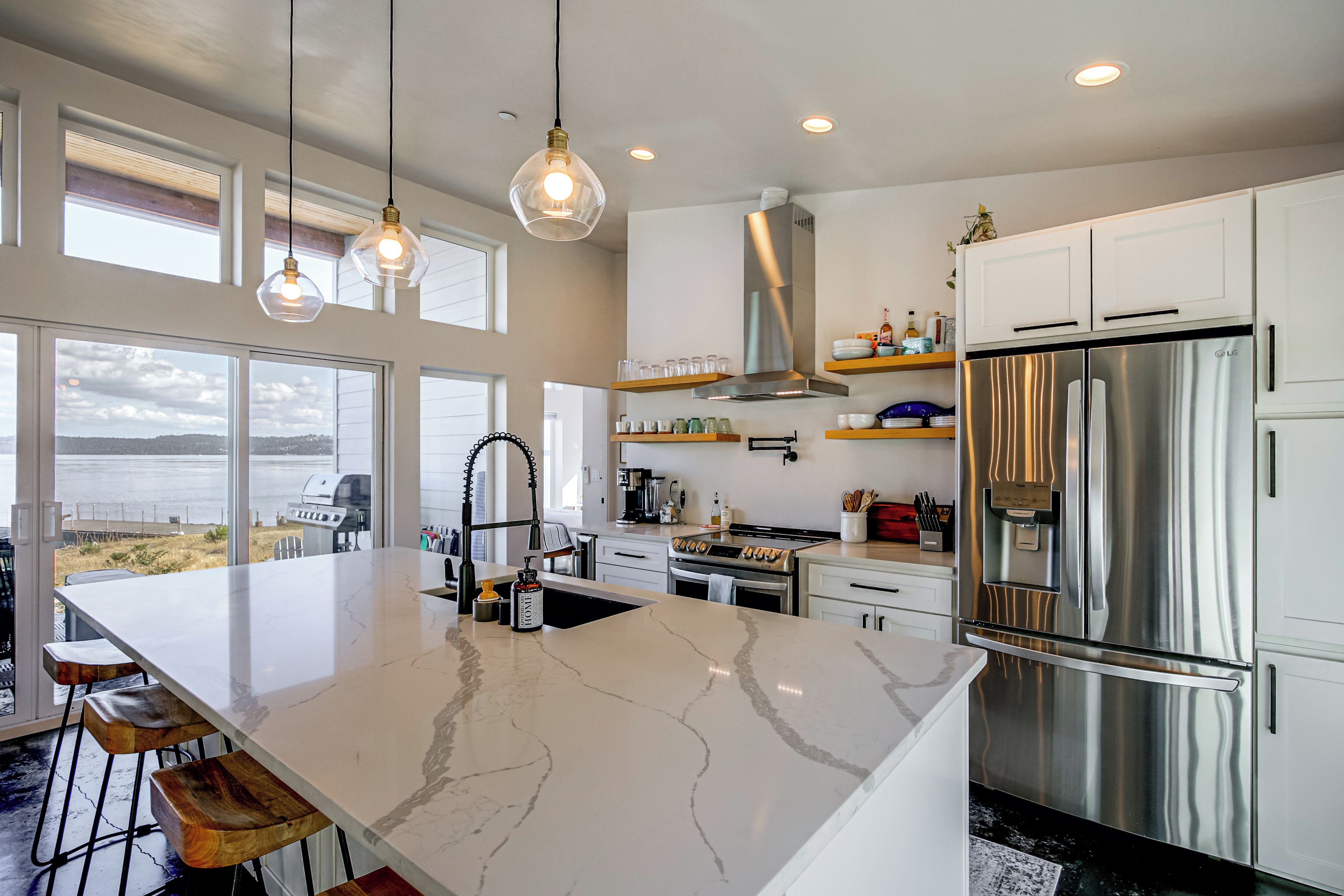 A modern kitchen with a large island, stainless steel appliances, and a view of the outdoors.