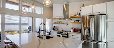 Une cuisine moderne dotée d’un grand îlot central, d’appareils électroménagers en acier inoxydable et offrant une vue sur l’extérieur.