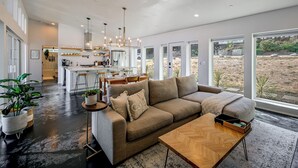 Un vaste espace de vie comprenant un grand canapé, une table basse et une vue sur un espace extérieur aménagé, grâce à de grandes fenêtres.