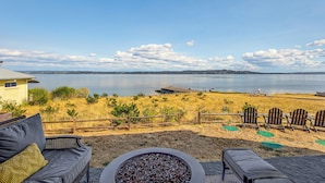 Une terrasse avec des meubles d’extérieur donnant sur un lac, une clôture en bois et une rive lointaine.