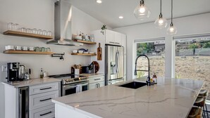 Une cuisine moderne dotée d’un grand îlot central, d’appareils électroménagers en acier inoxydable et offrant une vue sur l’extérieur.