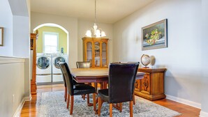 A dining area with a wooden table, four chairs, a chandelier, and a cabinet with a globe on top. - Modern Home w/ Private Deck & Yard in Indianapolis (Indianapolis)