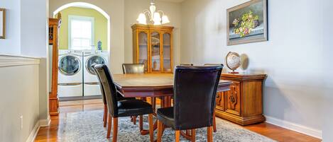 A dining area with a wooden table, four chairs, a chandelier, and a cabinet with a globe on top.