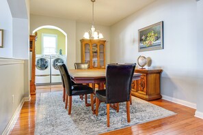 A dining area with a wooden table, four chairs, a chandelier, and a cabinet with a globe on top. - Modern Home w/ Private Deck & Yard in Indianapolis (Indianapolis)