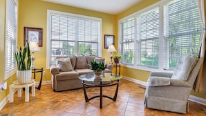 A living room with a sofa, armchair, and coffee table, large windows with blinds, and potted plants. - Modern Home w/ Private Deck & Yard in Indianapolis (Indianapolis)