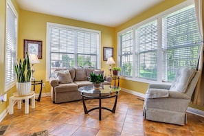 A living room with a sofa, armchair, and coffee table, large windows with blinds, and potted plants. - Modern Home w/ Private Deck & Yard in Indianapolis (Indianapolis)