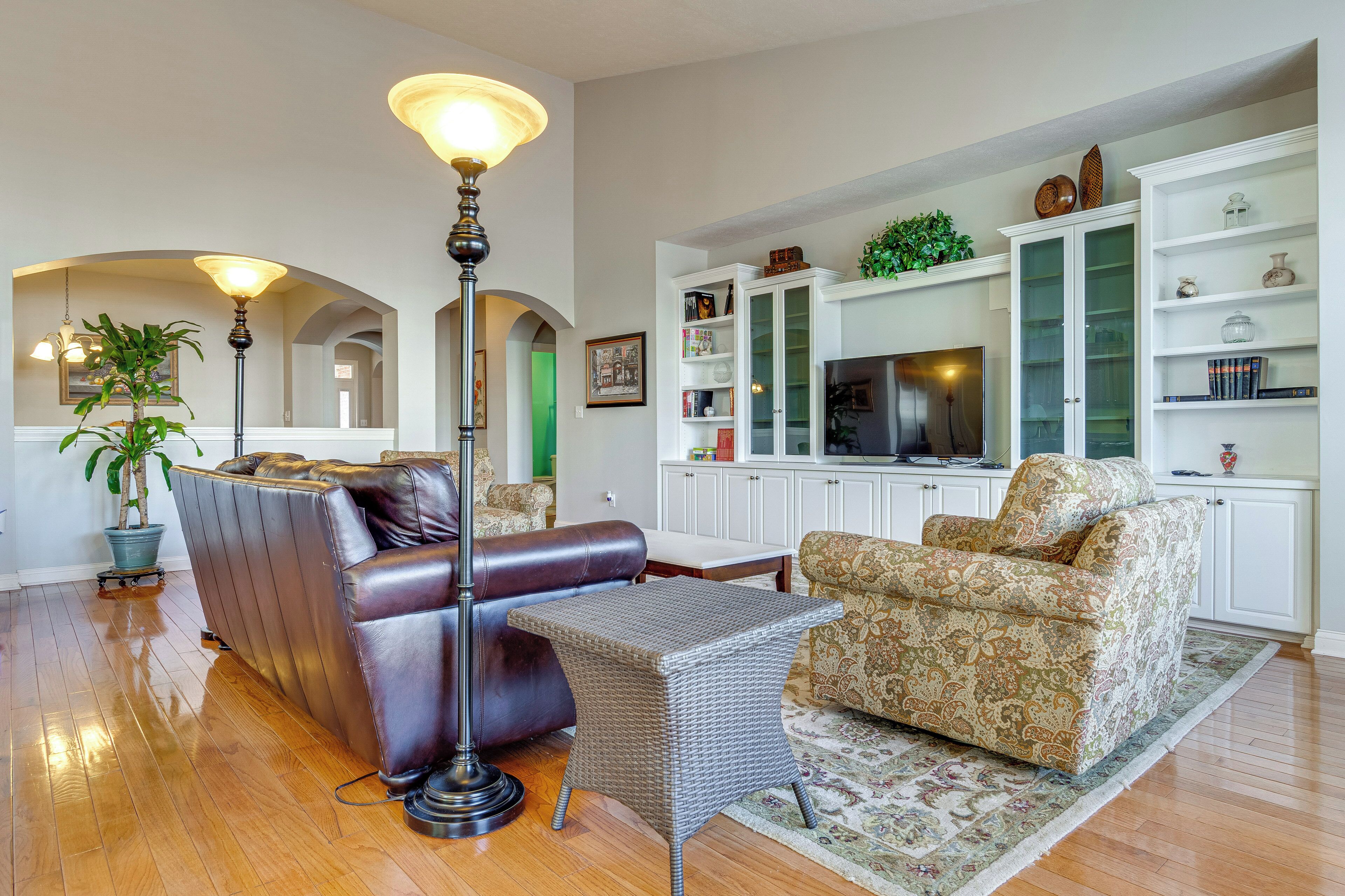 A living room with a leather sofa, a patterned armchair, a floor lamp, and a television on a cabinet.