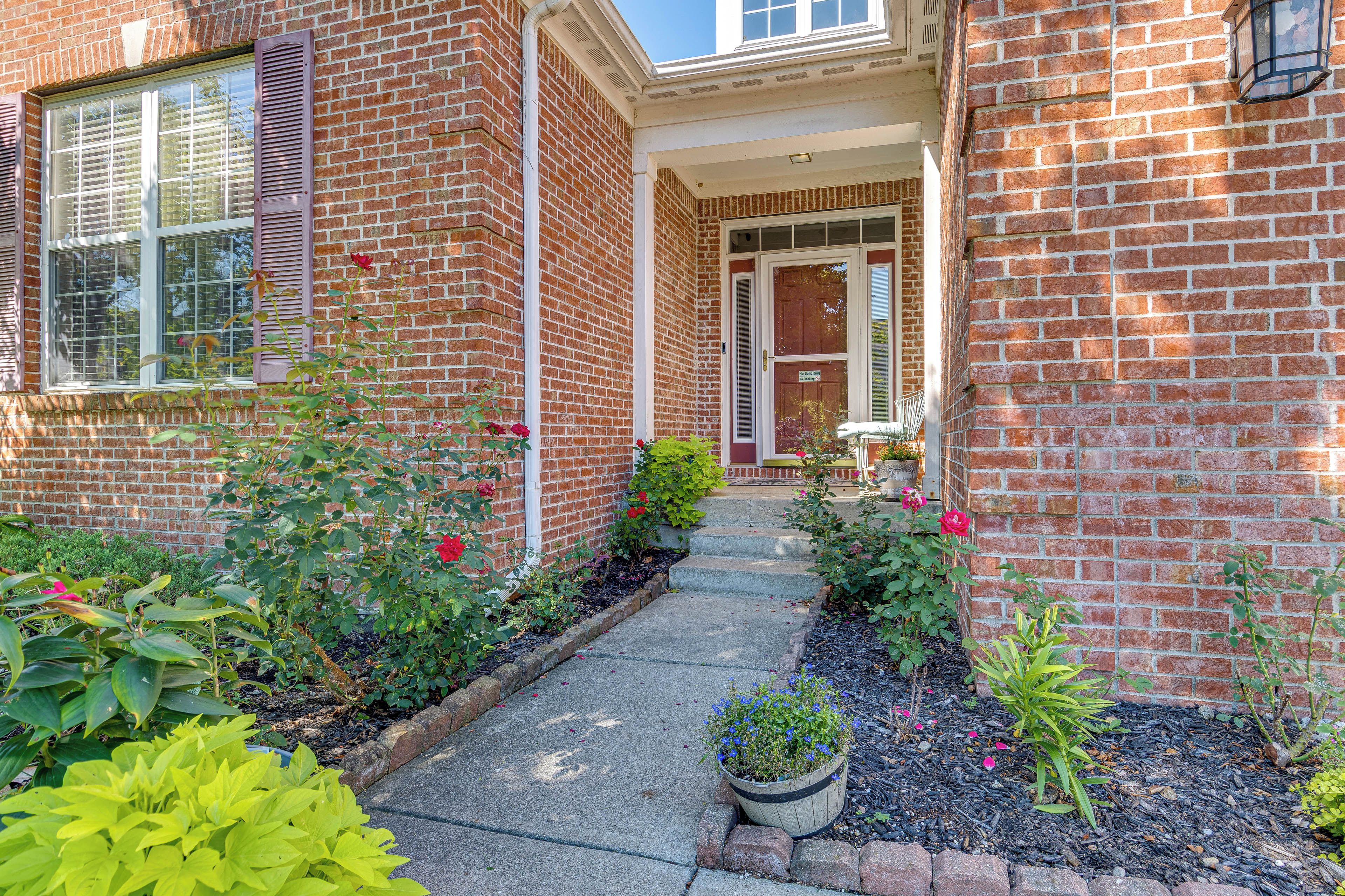 A brick house with a front porch, a door with a sign, and a garden with various plants and flowers.