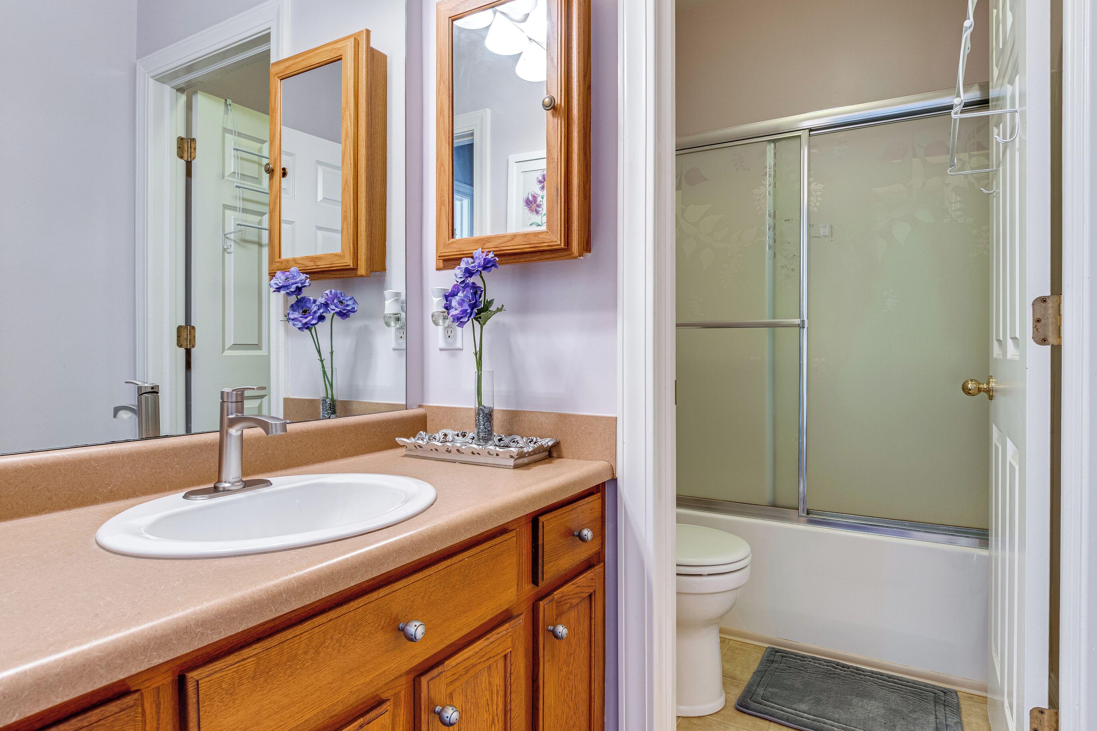 A bathroom with a sink, mirror, wooden vanity, and a shower area.