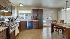 A kitchen with a stove, dishwasher, and a dining area with a table and chairs. - Extended East Tulsa Home w/ Fenced Yard (Tulsa)