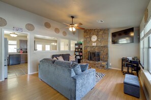 Ein Wohnzimmer mit grauem Sofa, Kamin aus Stein, Flachbildfernseher und Deckenventilator.