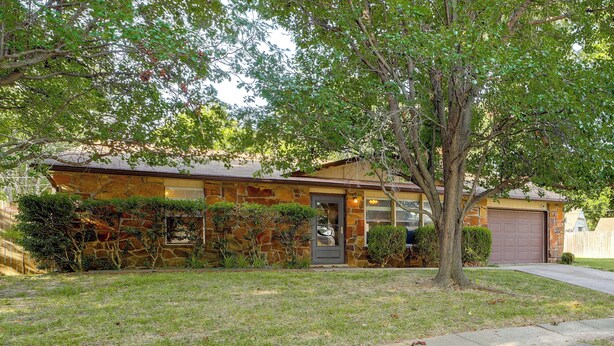 A single-story house with a stone facade, a front door, and a garage. - Extended East Tulsa Home w/ Fenced Yard (Tulsa)