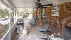A covered patio area with a grill, seating, and a ceiling fan.
