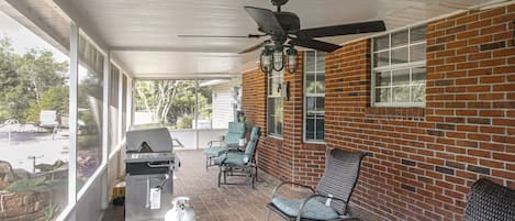 A covered patio area with a grill, seating, and a ceiling fan.