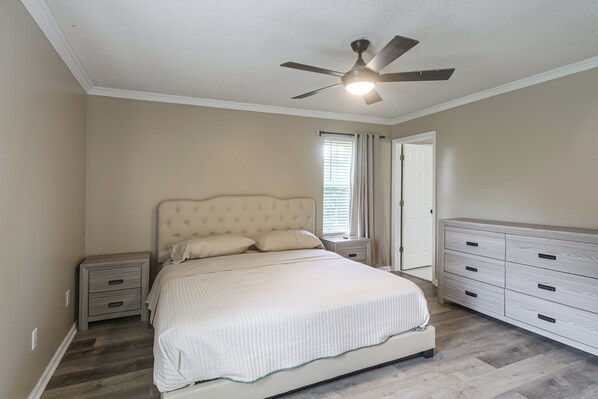 A bedroom with a bed, nightstands, a dresser, a ceiling fan, and a window with blinds.