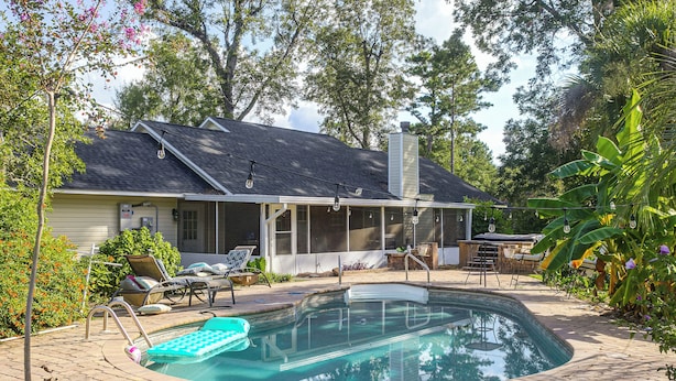 A backyard with a swimming pool, lounge chairs, and a covered patio area.