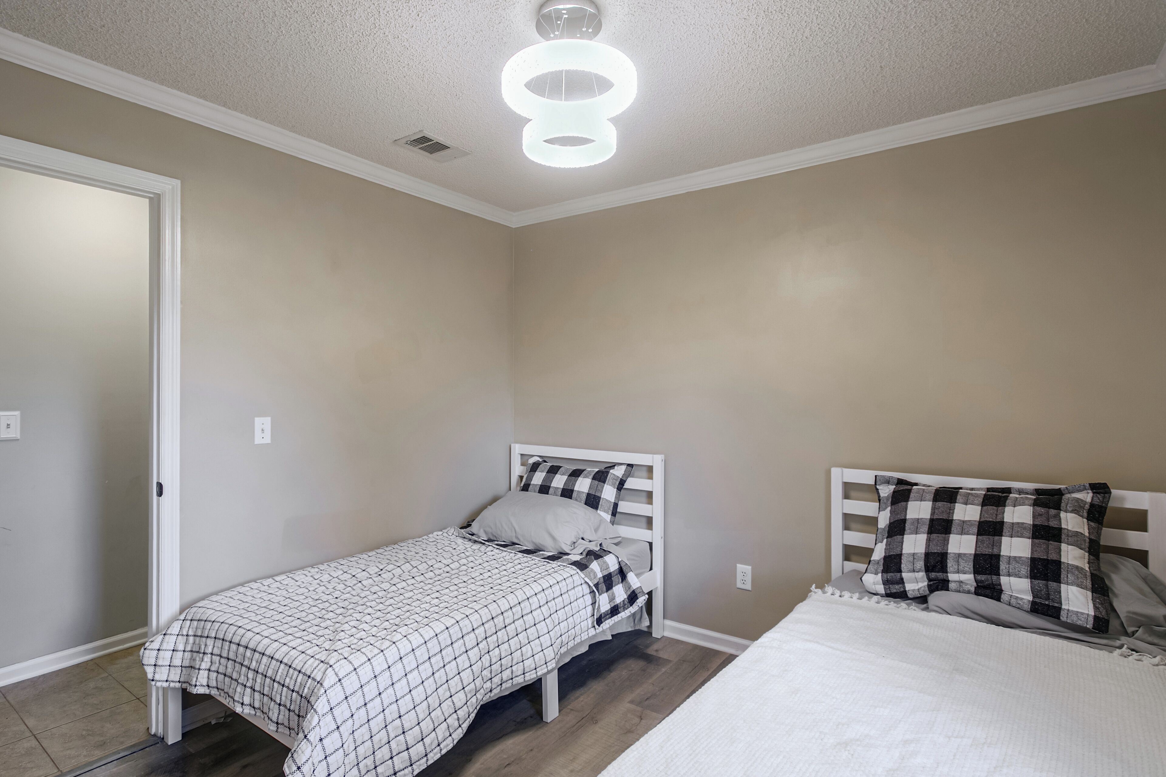 A bedroom with a single bed, a second smaller bed, a white ceiling light, and a door.