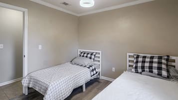 A bedroom with a single bed, a second smaller bed, a white ceiling light, and a door.